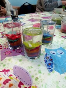 Zdjęcie przedstawia trzy kolorowe świece żelowe w szklanych naczyniach.