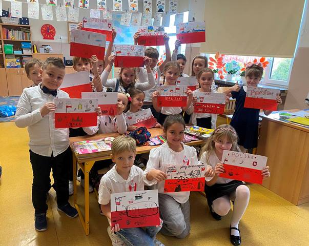Uczniowie klasy 2a w strojach galowych z podczas zajęć projektowych związanych z odzyskaniem niepodległości prezentujący wykonane flagi Polski.